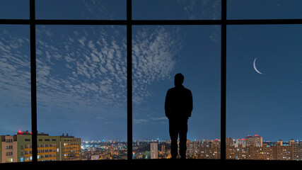 The man standing near the window against the night city