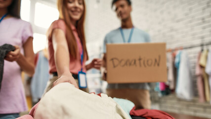 Young volunteers sorting, packing clothes in cardboard boxes, working on donation project indoors,...