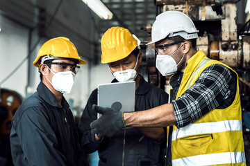 team engineer mechanic man wearing protective face mask and checking plan on tablet for maintenance metal machine at factory, teamwork concept