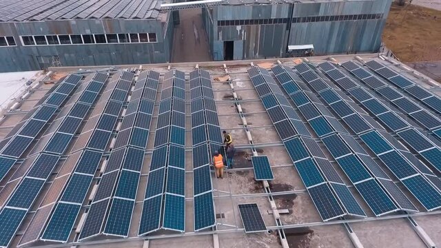 Installing solar panels on the foof of plant or factory. Additional source of electricity. Green energy. Video from the top.
