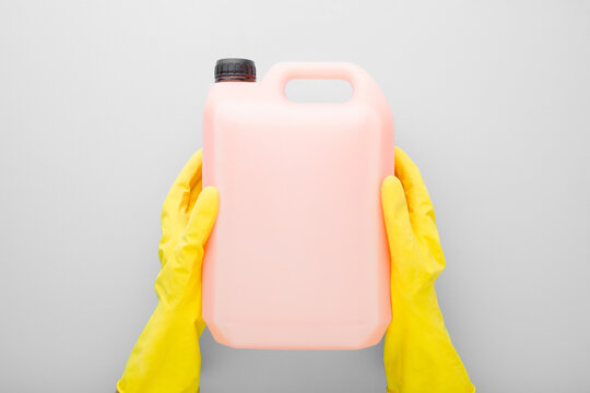 Hands in rubber protective gloves and 5 L plastic container on gray table background. Detergent for different surfaces in kitchen, bathroom and other rooms or washing liquid for dishes. Top down view.