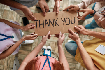 Top view of diverse young volunteers holding card with Thank you lettering while standing in...