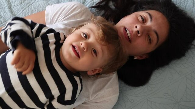 Mom and child boy lying in bed looking to camera