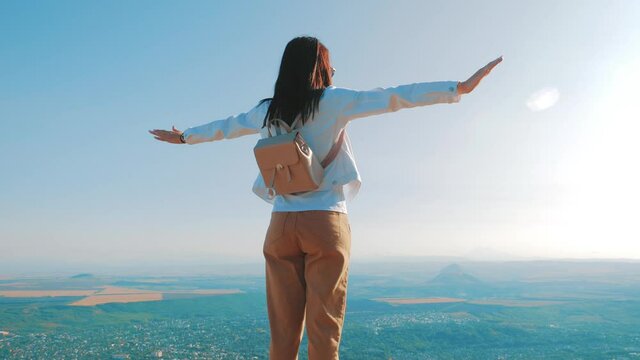 Happy traveler girl with a successful emotion by raise two arms over her head. Cheering successful woman hiker open arms on mountain top. Tourism, traveling and healthy lifestyle concept.