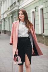 Fototapeta premium young stylish beautiful woman walking in street, wearing pink coat, purse, white shirt, black skirt, fashion outfit, autumn trend, smiling happy, accessories