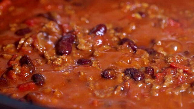 Cooking chili con carne in a frying pan. The bean stew is boiling.