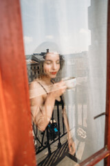 young beautiful woman with a cup of fragrant coffee standing by the window