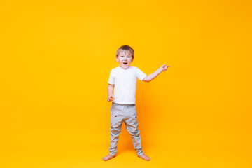 Fototapeta na wymiar Cute boy on yellow background points with his hand to the side, photo for advertising product