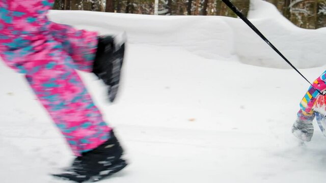 woman in warm suit runs taking daughter for ride on inflatable sledge on winter day closeup slow motion