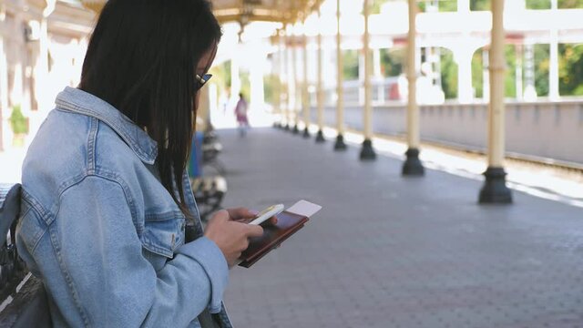 Young woman with phone in hand waiting on railway station for train.