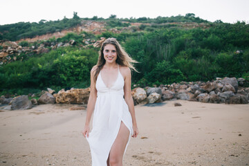 Fototapeta na wymiar Pretty positive woman in white dress walking along beach