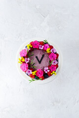 Mousse cake decorated with flowers in the form of a clock. Vertical orientation, top view, flat lay.