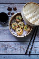Shrimp Shumai, dumplings are in bamboo steamer box or dim sum basket on bamboo table mat on  the wooden table in the Chinese restaurant during tea time party (yam cha) with close friend in New Year