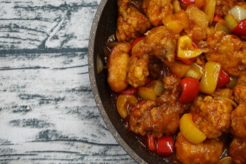 A dishes named Chicken sweet sour on a hot pan over vintage background. usually, people eat with rice.