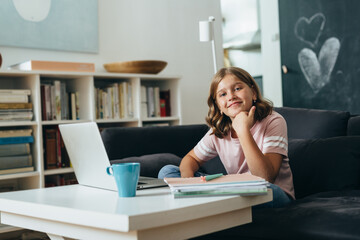 young girl sitting on sofa at her home and using computer for online education