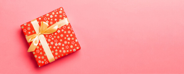 Top view Christmas present box with gold bow on living coral background with copy space