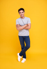 Handsome young Asian man smiling and standing with arms crossed over yellow background.