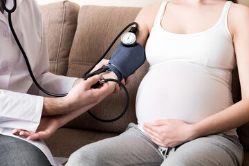 Young doctor is checking blood pressure of pregnant woman at home. High pressure problem during...