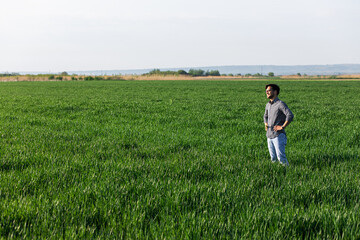 Fototapeta na wymiar Portrait of farmer standing in young wheat field examining crop.