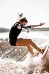 athletic woman stand on surf style wakeboard and ride up on splashed river wave.