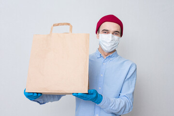 Fototapeta na wymiar Courier in a medical mask shows paper bag. Portrait, white background, copy space, concept of safe delivery goods.