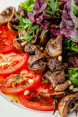Mushroom and tomato salad dressed with pesto sauce and pine nuts. Serving food in a restaurant on a white plate.
