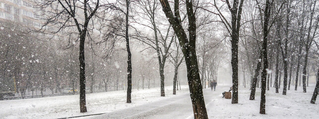 The first snow falls on a Park bench. Snow storm, snowstorm in the city. The first snow on a dark path and footprints on it. Heavy snowfall in the Park, large snowflakes fall on the sidewalk. © ru4eek