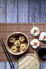 Shrimp Shumai, dumplings are in bamboo steamer box or dim sum basket on bamboo table mat on the wooden table with minced pork buns restaurant during tea time party (yam cha) with friend in New Year