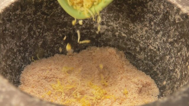 Close-up of lemon zest falling into the stone mortar with brown sugar and salt in slow motion