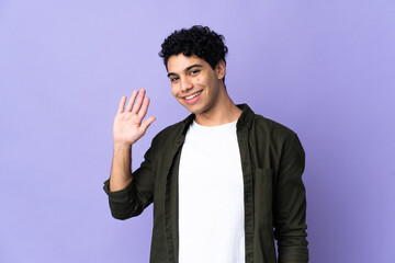 Young Venezuelan man isolated on purple background saluting with hand with happy expression