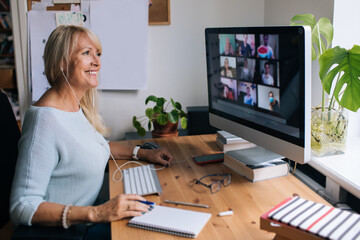 Smiling mature woman having video call via computer in the home office. Online team meeting video...