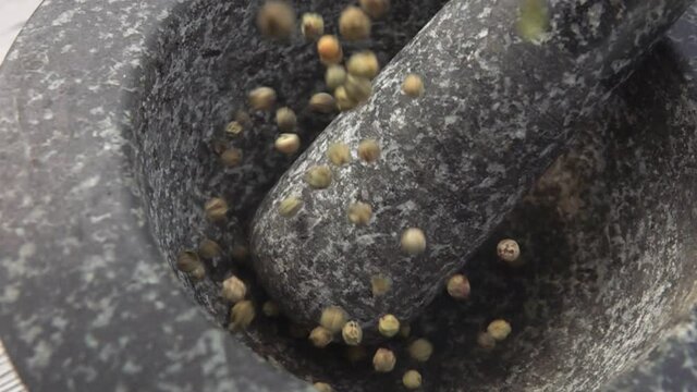 Green peppercorns are falling into the grey stone mortar in slow motion