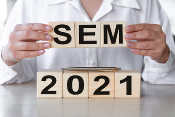 SEM 2021 - text on wooden cubes on a wooden table. Hands of businesswoman as the background. Business financial concept.