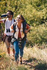 A young couple climbs a mountain, a beautiful day in nature, she carries a backpack for hiking while he drinks water