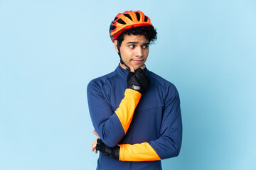 Venezuelan cyclist man isolated on blue background having doubts and thinking