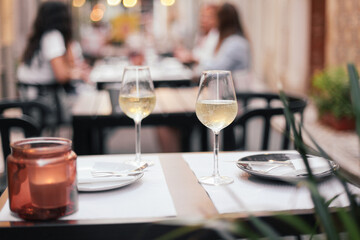 Two glasses of white wine on a table in an outdoor terrace, romantic dinner date with evening cozy lights