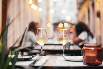 Two glasses of white wine on a table in an outdoor terrace, romantic dinner date with evening cozy lights
