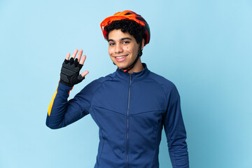 Venezuelan cyclist man isolated on blue background saluting with hand with happy expression
