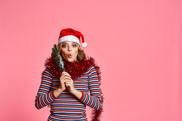 woman with christmas tree branches in hands red tinsel and festive hat pink background cropped view