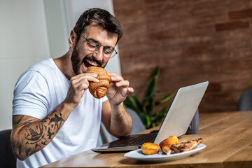 Young man sits alone in front of a laptop during the morning, has breakfast and prepares for online work
