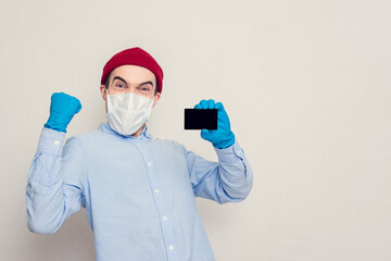 Fototapeta na wymiar Guy in a medical mask shows a card and rejoices in victory or good news, portrait, copy space