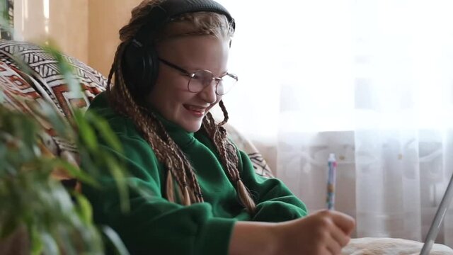 Teenager girl in glasses and headphones having lesson with online teacher. Child doing school homework talking with tutor. Kid learning foreign languages using laptop. Distance Homeschooling education