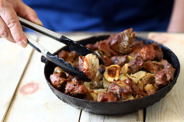 Selective focus. A man eats pieces of meat from a frying pan. Frying pan of fried meat.