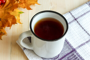 Tea in white cup with autumn leaves on white wooden table