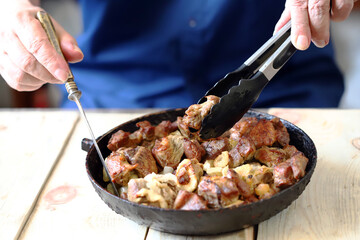 Selective focus. A man eats pieces of meat from a frying pan. Frying pan of fried meat.