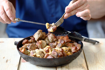 Selective focus. A man eats pieces of meat from a frying pan. Frying pan of fried meat.