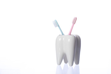 Two colorful toothbrushes in tooth-shaped holder. White decorative tooth, blue and pink toothbrushes. shiny toothbrush keeper isolated on white background copy space. Family without kids, childfree - Powered by Adobe
