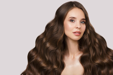 Fototapeta premium Portrait of a beautiful brunette woman with wavy hair and makeup. On a gray background
