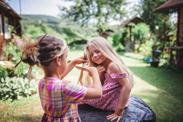 Girl brushing hair of her younger sister on the backyard of wooden house, healthy beauty