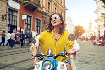 young beautiful hipster woman riding on motorbike city street, summer europe vacation, traveling, smiling, happy, having fun, sunglasses, stylish outfit, adventures, positive, waving hand
